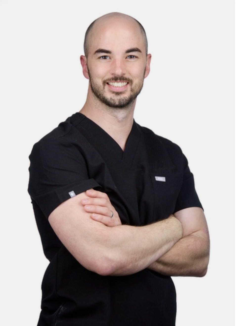 Bradley C. Tenny, nurse practitioner and founder of Reach Aesthetics, wearing black medical scrubs with arms crossed.